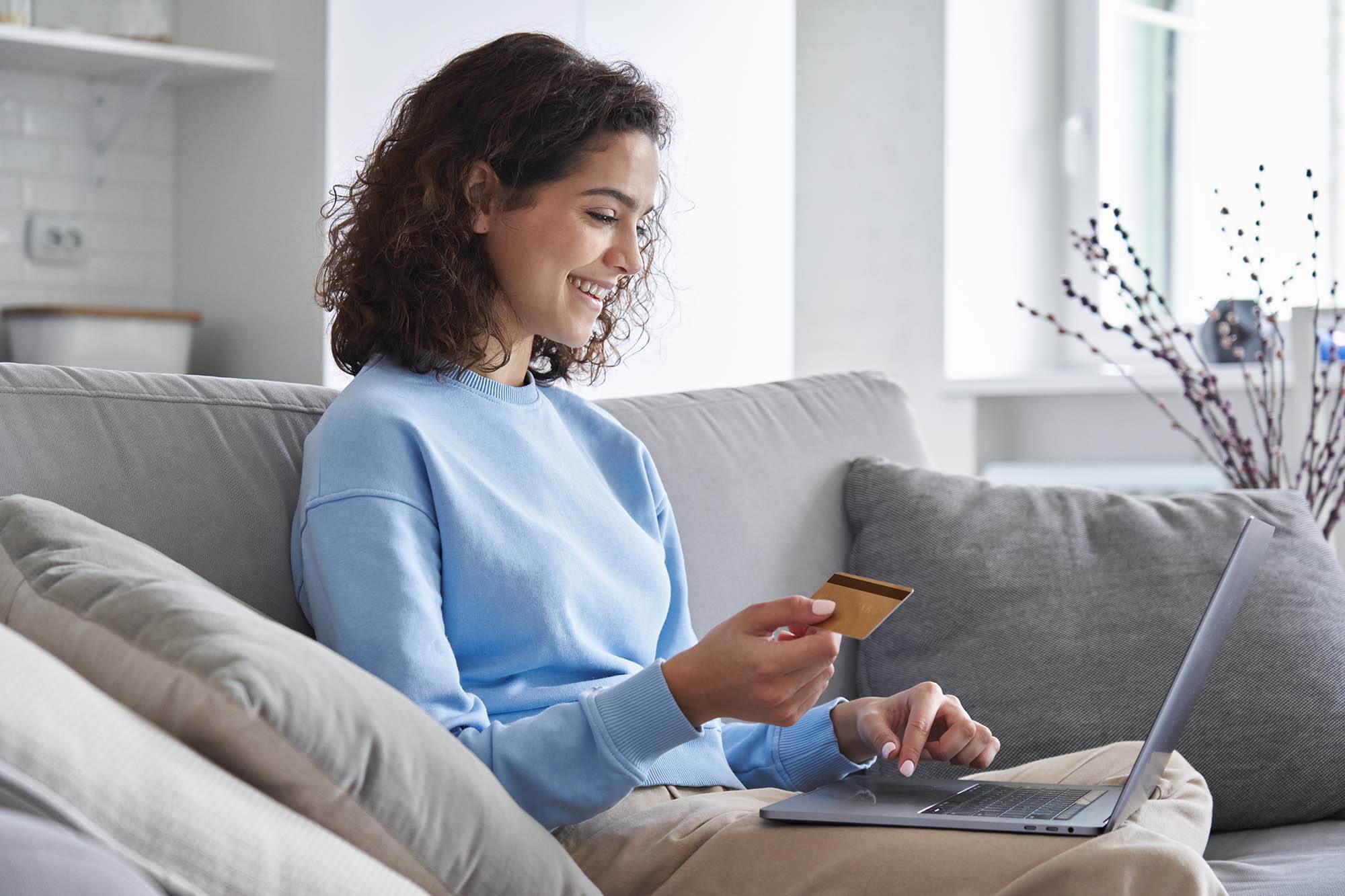A woman smiling as she uses her laptop to perform a balance transfer on her new low-rate credit card.