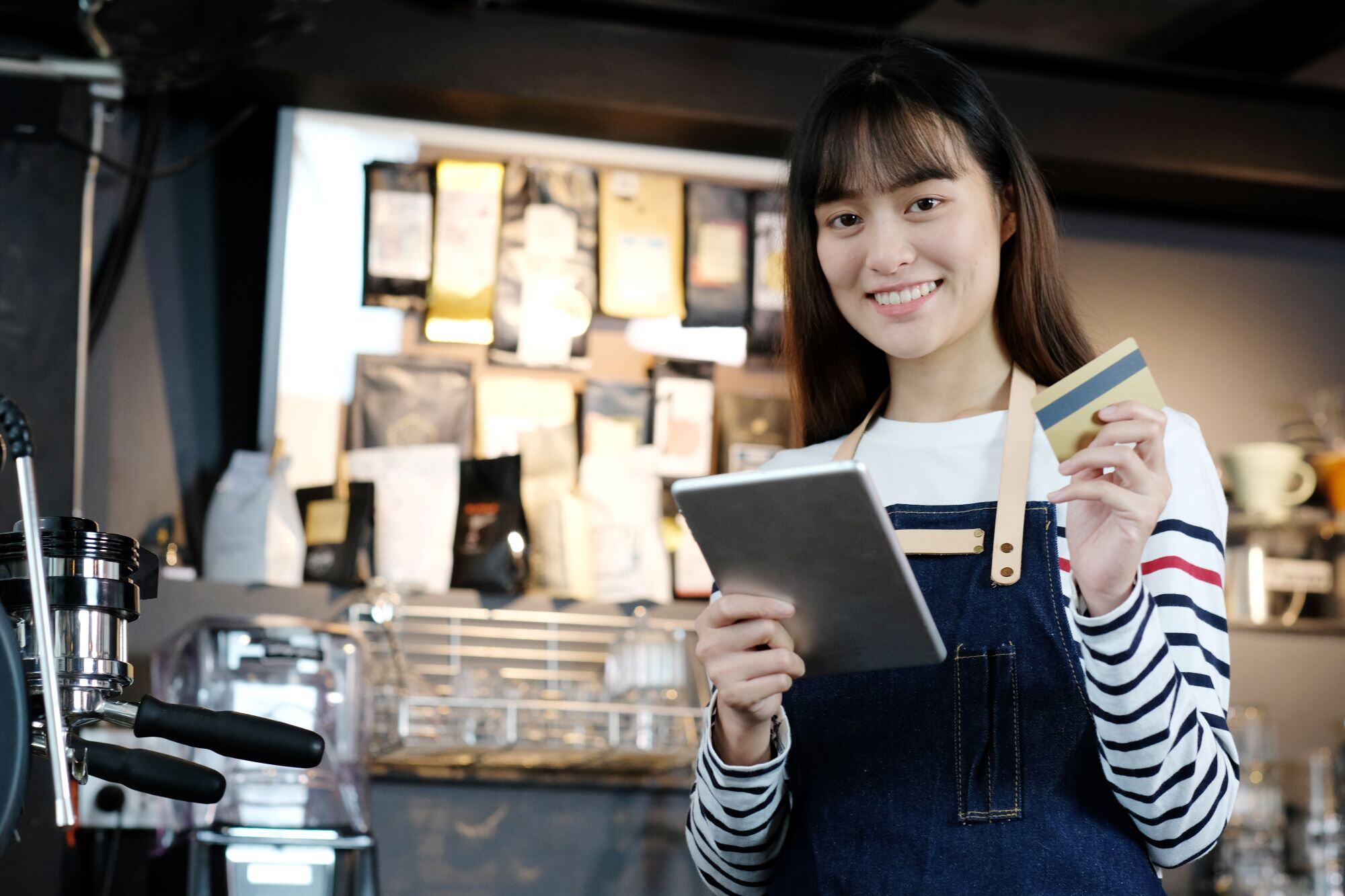 Young female coffee shop owner uses her business debit card to buy supplies.