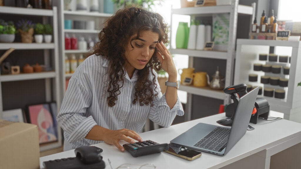 A younger female business owner uses a hand calculator to determine if she has saved enough for her business this month.